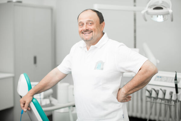 Zahnarzt steht freundlich lächelnd in moderner Zahnarztpraxis mit Behandlungsstuhl.