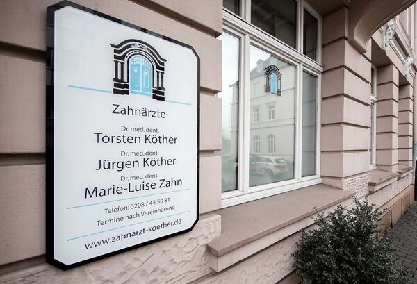 Praxisschild einer Zahnarztpraxis mit Namen der Zahnärzte an einer Hauswand in der Stadt.