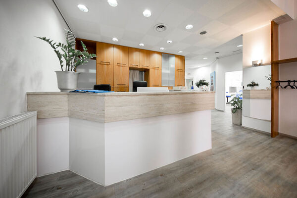 Moderne, helle Rezeption einer Arztpraxis mit Holztheke und Pflanzen im Empfangsbereich.