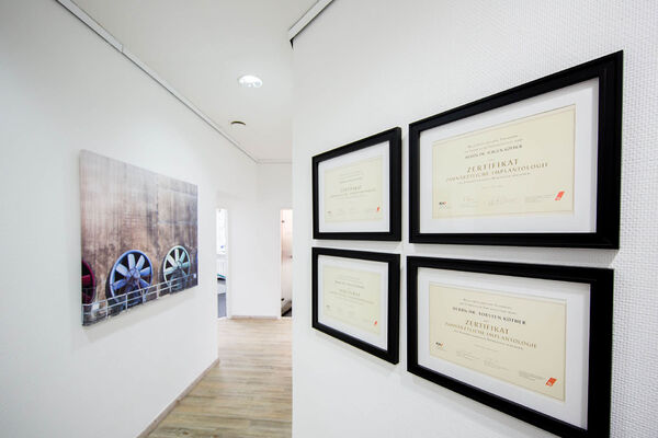 Vier Zertifikate zur zahnärztlichen Implantologie hängen gerahmt an einer weißen Wand.