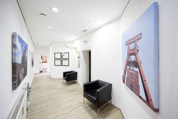 Heller Flur einer Zahnarztpraxis mit Bildern, Auszeichnungen, Wartebereich und moderner Einrichtung.