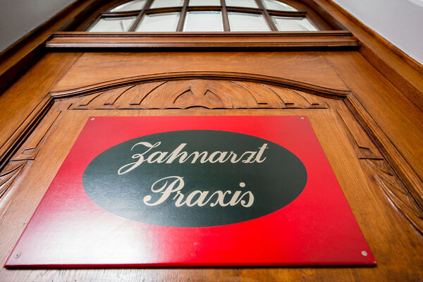 Rotes Zahnarztpraxis-Schild mit weißer Schrift an einer hölzernen Tür im Eingangsbereich.